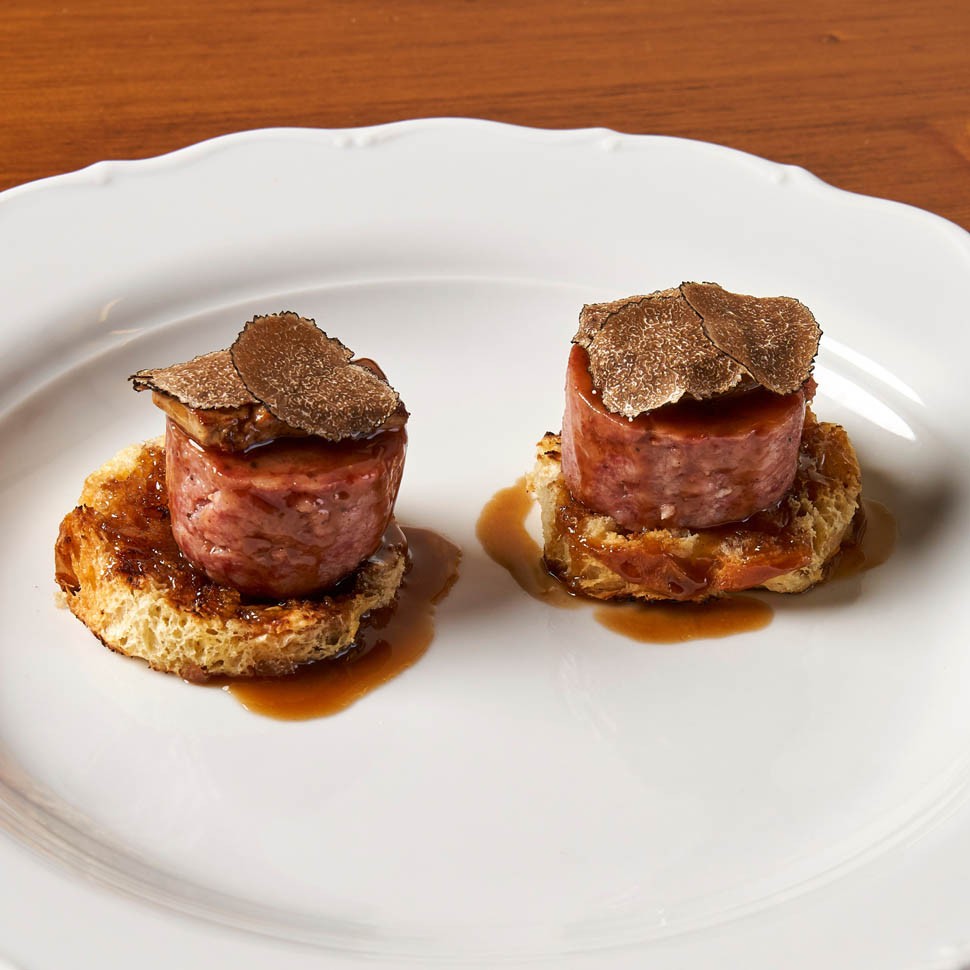 Due medaglioni di cotechino su una base dorata, con lamelle di tartufo nero e fondo bruno, su un piatto bianco