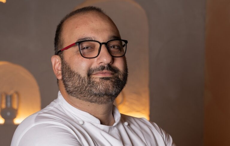 Lorenzo Barsotti in giacca bianca da chef e occhiali, sorride davanti alle nicchie illuminate della sala