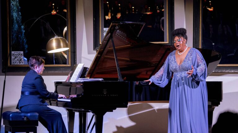 Una cantante in abito azzurro canta accanto alla pianista al pianoforte a coda durante Laurus Florentiae di Mascarade Opera