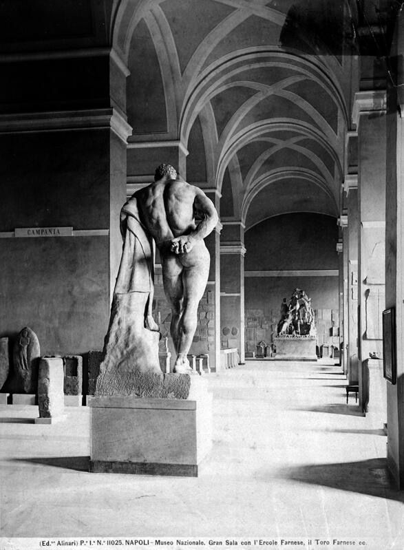 L'Ercole Farnese di spalle sotto una galleria ad archi del Museo Nazionale di Napoli, in una foto d'epoca in bianco e nero