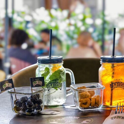 Due drink nei boccali di New Bridge con olive e stuzzichini su un tavolo all’aperto del New Bridge Pizza Club a Firenze