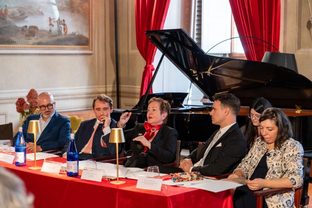 I relatori seduti a un tavolo rosso, con un pianoforte a coda alle spalle, alla presentazione della stagione a Firenze
