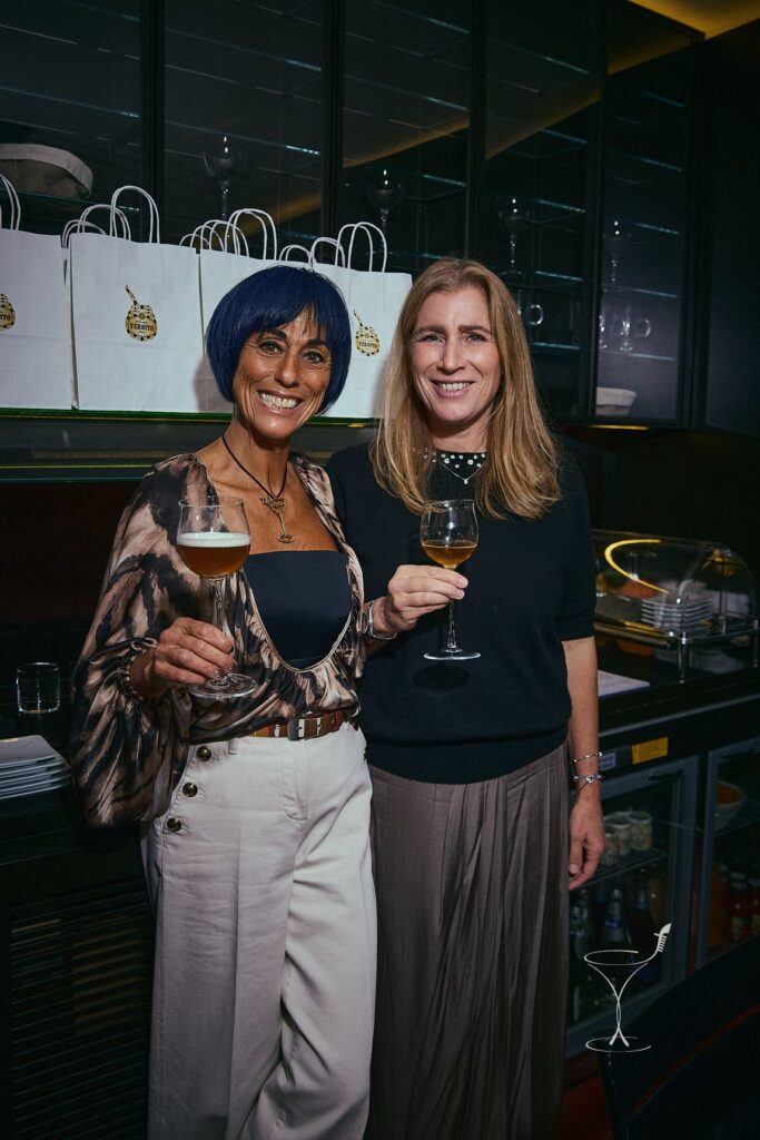 Paola Mencarelli, coi capelli blu, e Karin Cristiana Romano sorridono col calice in mano in un bar in penombra