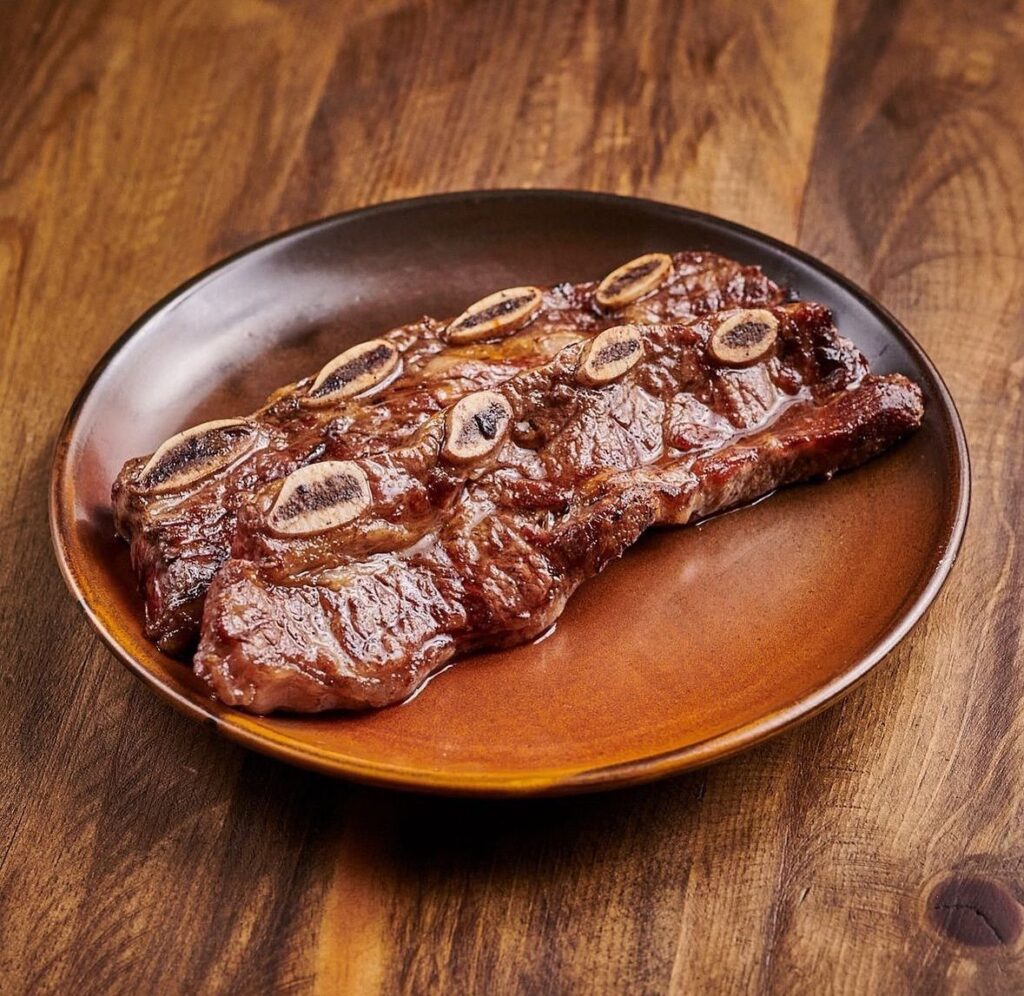 Costine di manzo con l’osso, tagliate di traverso e cotte alla brace, su un piatto di terracotta sopra un tavolo di legno