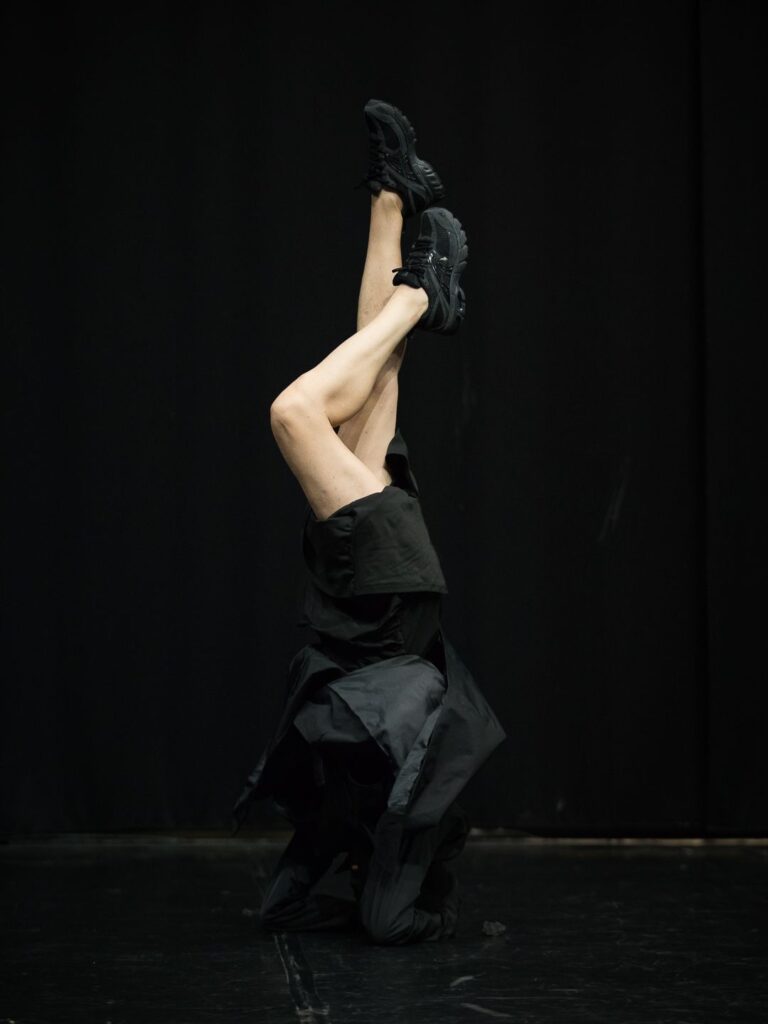 Sentimental di Cristina Kristal Rizzo: una danzatrice capovolta, gambe nude tese verso l'alto e abito nero, su un palco buio