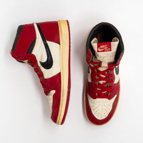 Un paio di Nike Air Jordan 1 del 1985 bianche, rosse e nere, una vista di profilo e una dall’alto, su fondo bianco