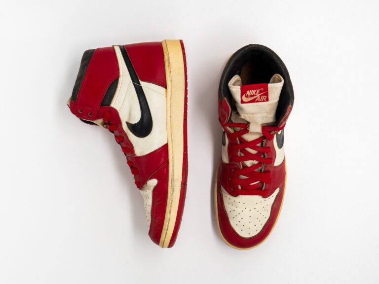 Un paio di Nike Air Jordan 1 del 1985 bianche, rosse e nere, una vista di profilo e una dall’alto, su fondo bianco
