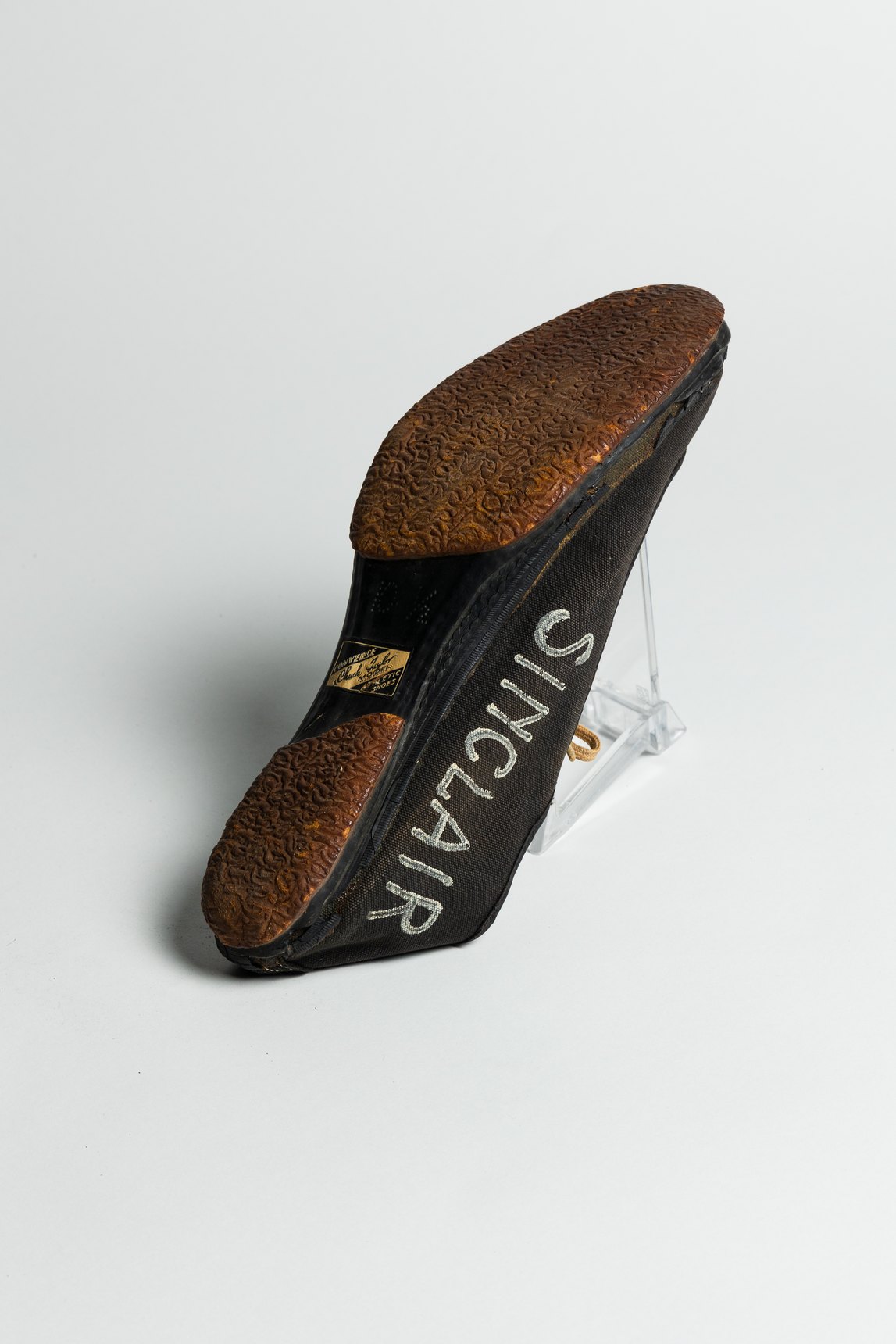 Black Converse running shoe seen from its worn sole, with the word SINCLAIR on the inner side of the upper