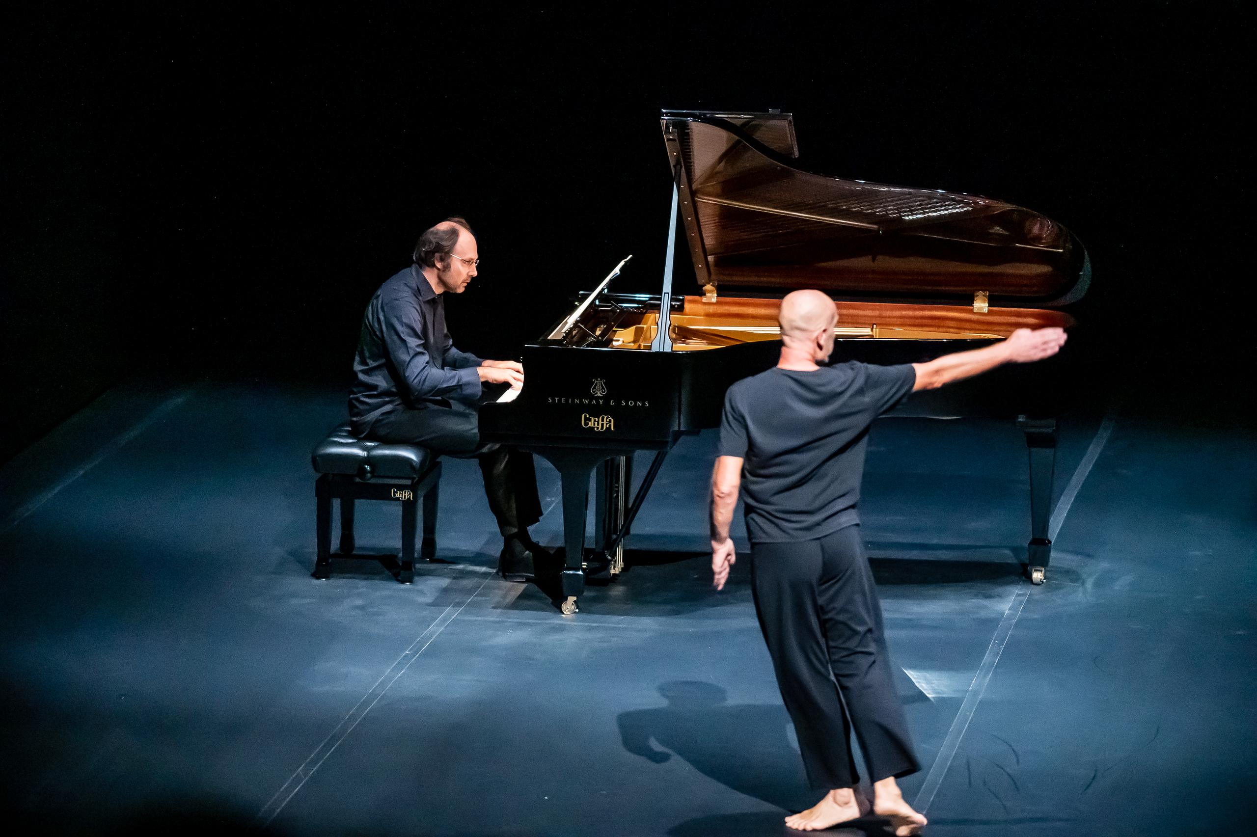 Virgilio Sieni in Solo Goldberg Variations: a piedi nudi, un braccio teso, accanto a un pianista al pianoforte a coda