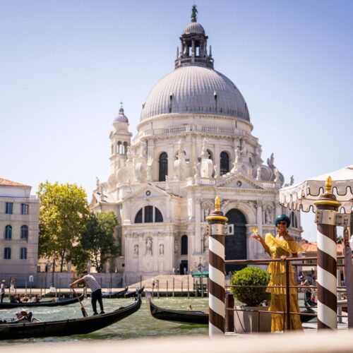 Paola Mencarelli in abito giallo su un pontile del Canal Grande, davanti alla basilica della Salute e alle gondole