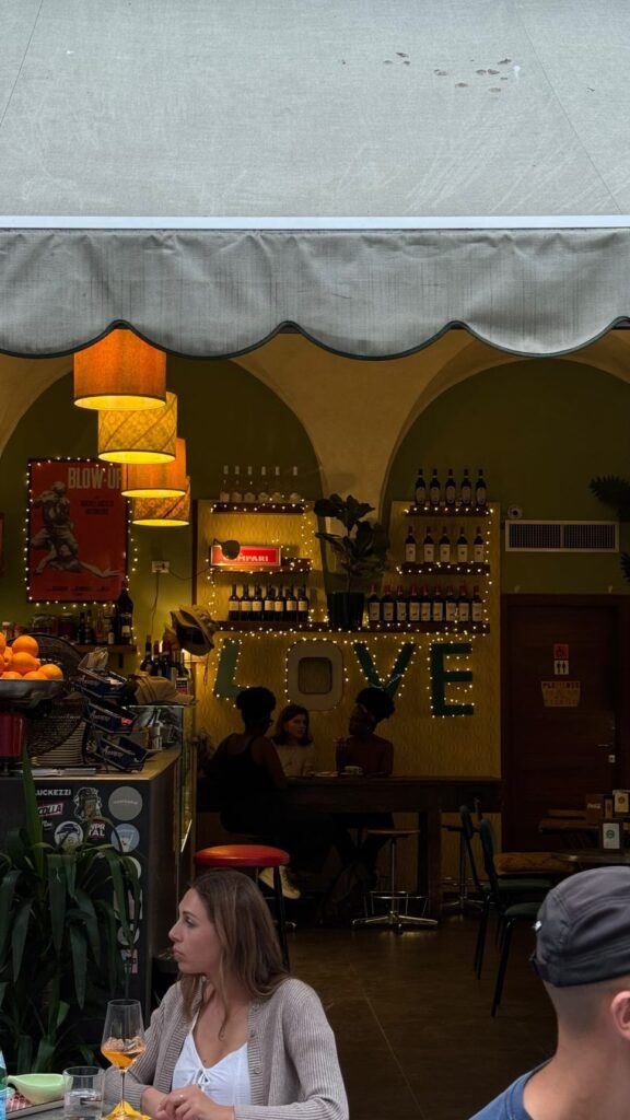 Il bancone di Vintage Cafe a Firenze, con lampade gialle e la scritta LOVE luminosa, e clienti seduti fuori sotto la tenda